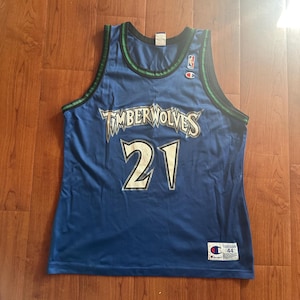 Puede incluir: Camiseta de baloncesto azul Champion Timberwolves con el número 21 en blanco. La camiseta tiene ribetes verdes y negros alrededor del cuello y las sisas. El logotipo de los Timberwolves está en el pecho.