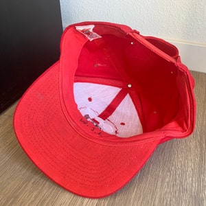 May include: Red baseball cap with a white logo and the text "W.J.L." embroidered on the front.