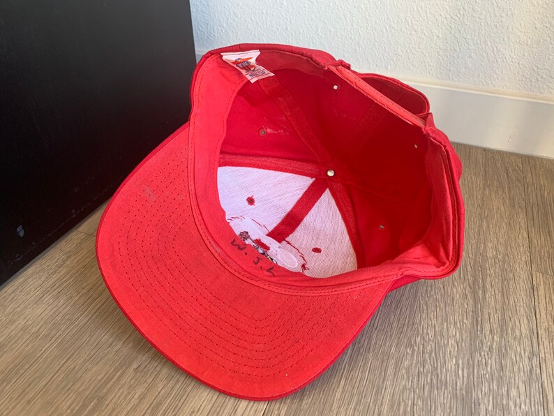 May include: Red baseball cap with a white logo and the text "W.J.L." embroidered on the front.