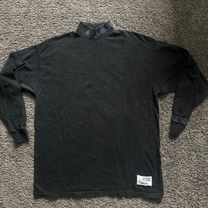 May include: Black long-sleeve mock neck shirt with a purple "LAKERS" logo on the collar and a white "NBA" tag on the bottom right side.