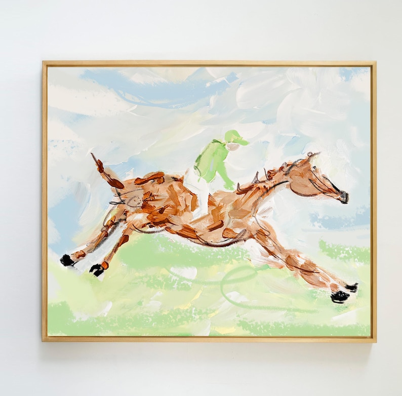 A framed abstract painting of a horse and jockey in motion hanging on a plain white wall.