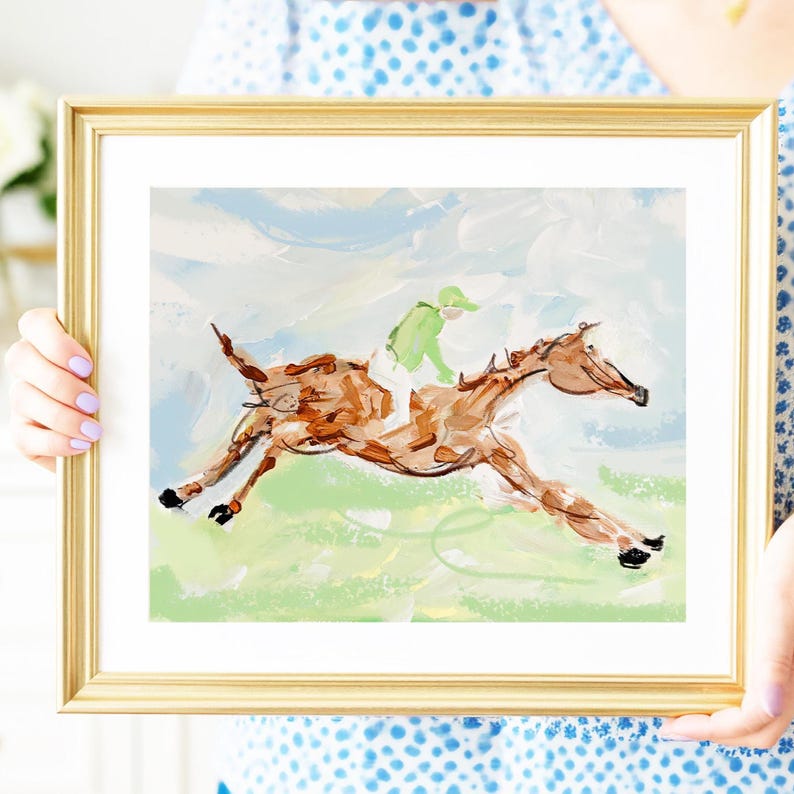 A person wearing a blue patterned shirt holds a framed painting of a galloping horse.