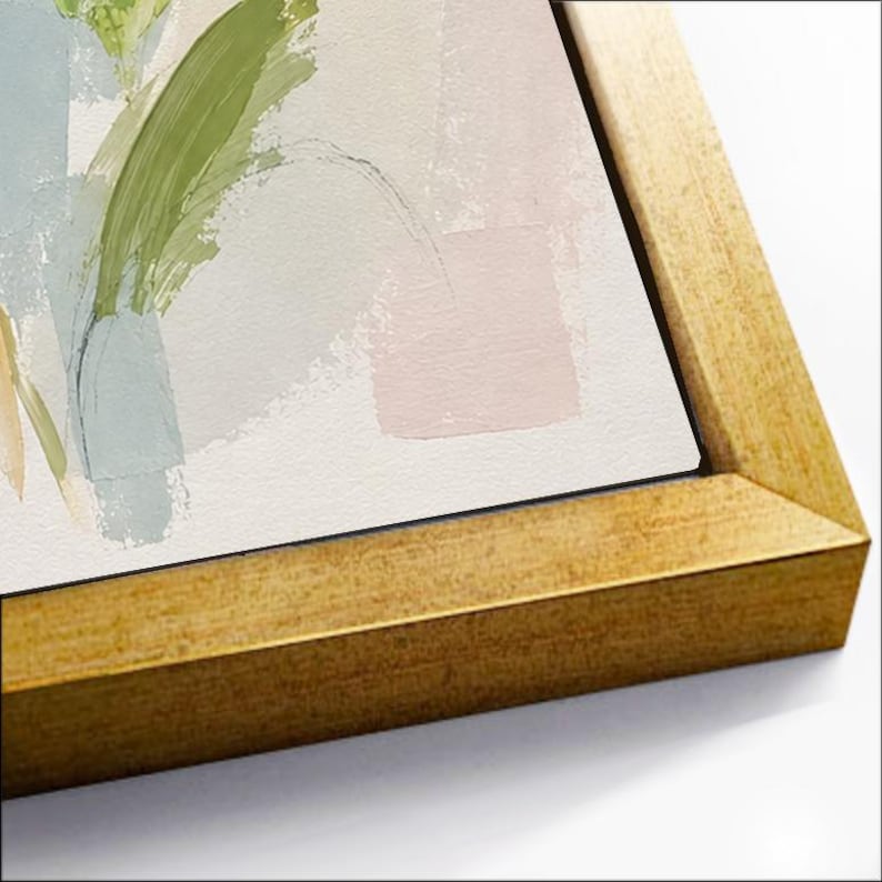 May include: A framed canvas print featuring abstract brushstrokes in shades of sage green, soft blue, and pale pink on a white background. The artwork is encased in a metallic gold frame with a textured finish, viewed from an angled perspective.