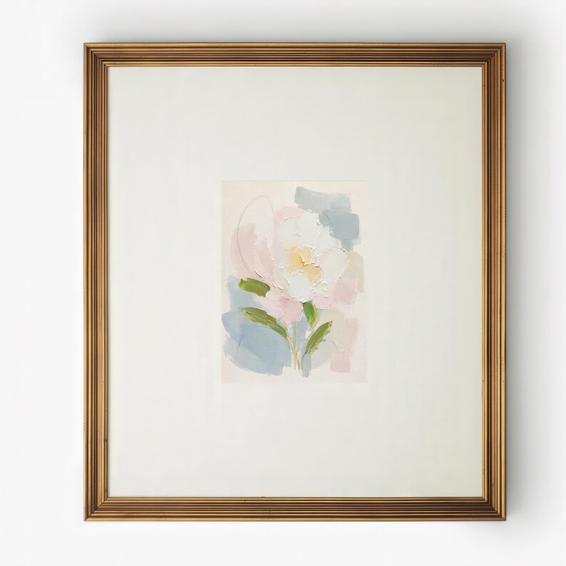 May include: A framed painting featuring an abstract floral subject with thick, textured brushstrokes in shades of white, soft pink, pale yellow, and muted blue, set within a wide off-white mat and a metallic gold-toned rectangular frame.