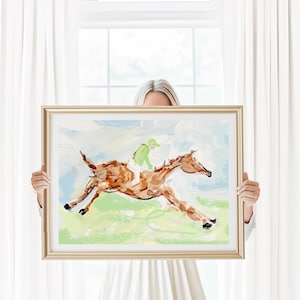 A person holds up a framed impressionist horse painting in front of a white window with sheer curtains.