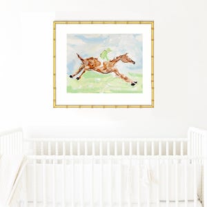 The framed horse and jockey painting hangs on a white wall centered directly above a white crib.
