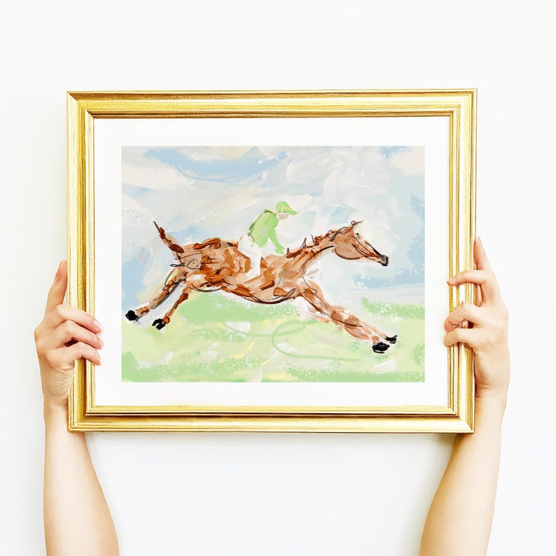 A person's hands hold a framed impressionist horse painting against a plain white background.