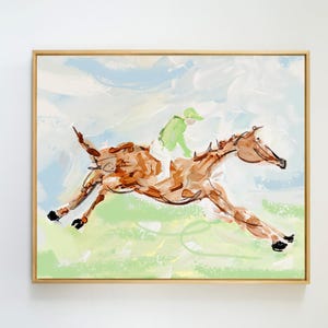A light wood-framed painting of a brown horse and jockey galloping across a grassy landscape.