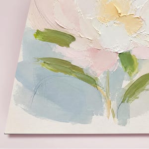 May include: An oil painting on canvas featuring a large, textured floral bloom in shades of pale pink, cream, and soft yellow. The flower is accented by thick, visible brushstrokes of sage green leaves and stems set against a muted light blue background.