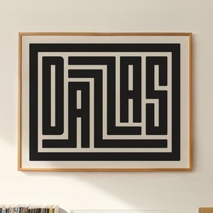 Puede incluir: Una impresión enmarcada en blanco y negro de la palabra "Dallas" en una fuente geométrica. La impresión está colgada en una pared blanca sobre un gabinete de madera con un tocadiscos, una planta y una pila de discos de vinilo.
