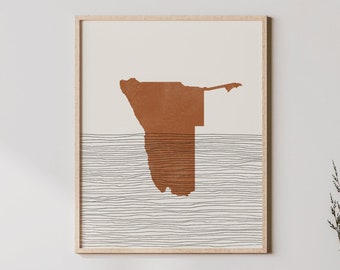 May include: A minimalist art print featuring a brown outline of Namibia on a white background with thin black lines. The print is framed in a light wood frame and hangs above a light wood cabinet with a woven rattan front.