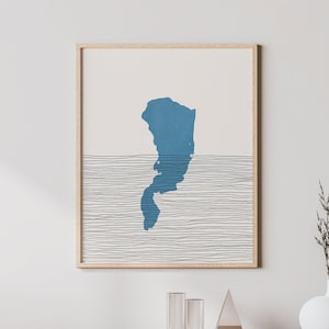 May include: A framed print of a blue island silhouette with a white background and black lines. The print is hanging on a white wall above a wooden cabinet with a woven rattan door.