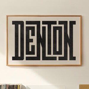 Könnte beinhalten: Ein gerahmter Schwarzweißdruck des Wortes "Denton" in einer modernen Schriftart, der an einer weißen Wand hängt. Ein Plattenspieler mit einem Stapel Schallplatten steht auf einem Holzregal unter dem Druck. Eine Schallplatte mit dem Text "Best of The Beach Boys" befindet sich auf dem Regal neben dem Plattenspieler.