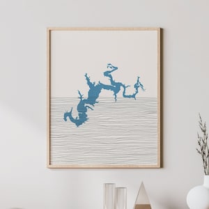 May include: A framed abstract art print with a blue organic shape above a horizontal line design. The artwork is displayed on a wall above a wooden cabinet with a vase and decorative items.