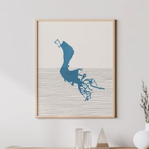 May include: A minimalist living room interior with a wooden console table, a chair, and a framed print of a blue silhouette of an island with a white background. The print is hanging on a white wall.