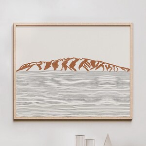 May include: A framed print of a minimalist line drawing of a mountain range with a brown silhouette against a white background. The mountain range is reflected in a series of thin, horizontal lines representing water.