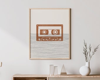May include: A minimalist poster with a brown cassette tape design on a white background. The cassette tape is partially submerged in a series of thin, horizontal lines. The poster is framed in a light wood frame and is hanging on a white wall.