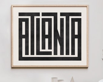 Könnte beinhalten: Ein Schwarzweißdruck mit dem Wort "ATLANTA" in einer geometrischen Schriftart. Der Druck ist in einem hellen Holzrahmen gerahmt und hängt an einer weißen Wand über einem Holzregal.
