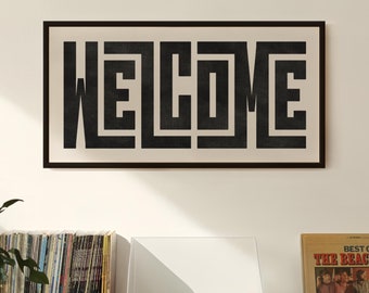 May include: A black and white framed print with the word "WELCOME" in a bold, geometric font. The print is hanging on a white wall above a wooden cabinet with a record player and a stack of vinyl records.