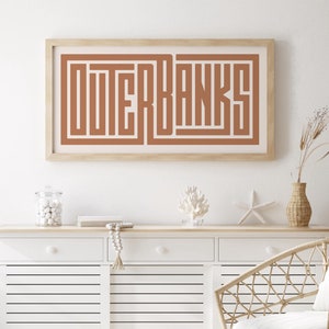 May include: A white cabinet with three drawers and slatted doors, a wicker chair with a white cushion, a framed print with the text "OUTER BANKS" in brown, a glass jar with white beads, a wooden starfish, and a vase with dried flowers.