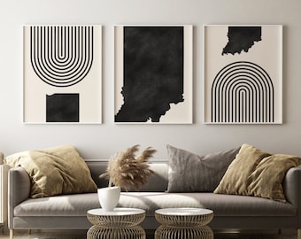 Puede incluir: Tres impresiones de arte abstracto en blanco y negro en marcos colgados en una pared blanca sobre un sofá gris con dos mesas auxiliares de metal dorado. El sofá tiene dos almohadas, una marrón y una dorada.