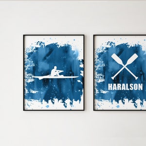 Peut inclure: Deux impressions aquarelle bleues avec des silhouettes blanches. L'impression de gauche représente une personne faisant du bateau à rames avec des rames. L'impression de droite représente deux rames croisées et le texte "HARALSON".