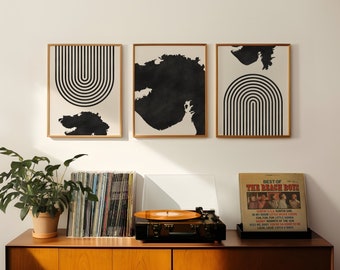 May include: Three framed black and white abstract prints with geometric shapes hang on a white wall above a wooden cabinet. A record player sits on the cabinet with a vinyl record of "Best of The Beach Boys" on top.