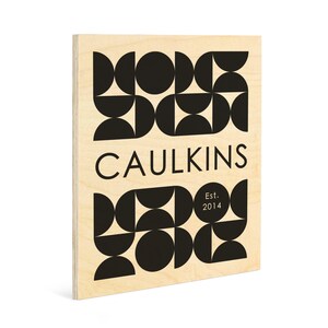 May include: A wooden sign with a geometric pattern in black and white. The text "CAULKINS" is centered on the sign, with "Est. 2014" below it.