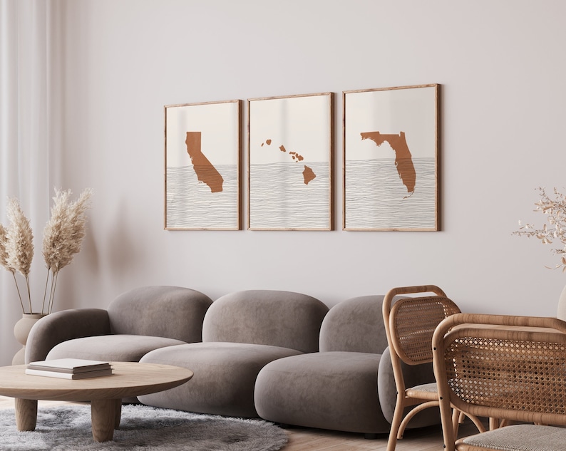 May include: Three framed prints of state outlines in a minimalist style. The prints feature the outlines of California, Hawaii, and Florida, each with a brown silhouette against a white background. The outlines are set against a backdrop of thin, white lines that resemble waves.