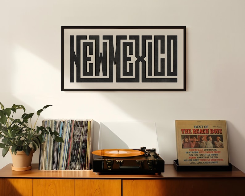 May include: A framed black and white print of the word "NEW MEXICO" in a maze-like design hangs above a record player and vinyl records. A "Best of The Beach Boys" album cover is displayed nearby.