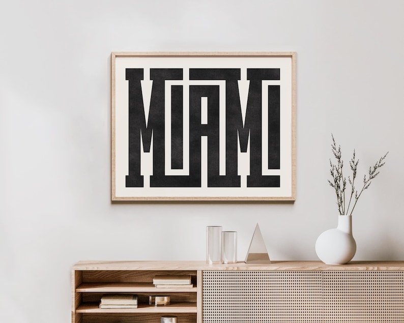 K&ouml;nnte beinhalten: Ein Schwarz-Wei&szlig;-Typografie-Druck mit dem Wort "MIAMI" in fetten Blockbuchstaben. Der Druck ist in einem hellen Holzrahmen gerahmt und h&auml;ngt an einer wei&szlig;en Wand &uuml;ber einem Holzregal.
