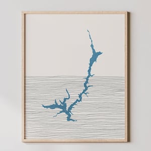 May include: A framed print of a blue lake outline with black lines resembling waves. The print is on a white background and has a light wood frame.