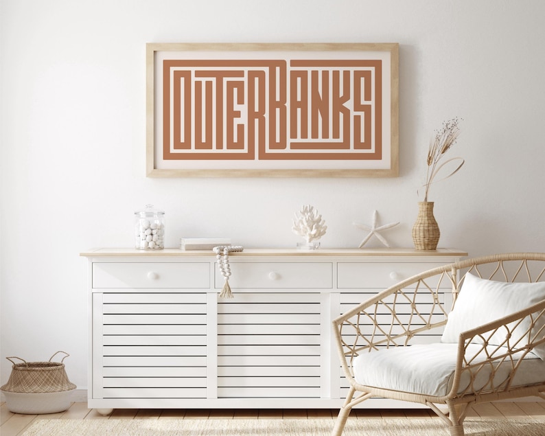 May include: A white cabinet with three drawers and slatted doors, a wicker chair with a white cushion, a framed print with the text "OUTER BANKS" in brown, a glass jar with white beads, a wooden starfish, and a vase with dried flowers.
