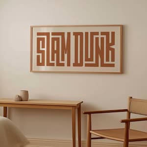 May include: A framed print with the text "SLAM DUNK" in a brown color. The print is hanging on a white wall above a wooden table and chair.