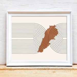 May include: A white framed print with a brown outline of the country of Lebanon. The outline is surrounded by black concentric circles.