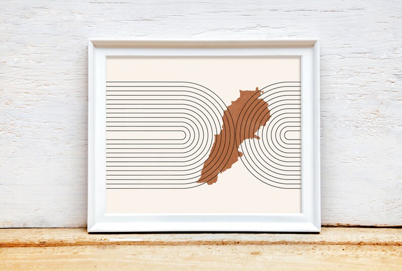 May include: A white framed print with a brown outline of the country of Lebanon. The outline is surrounded by black concentric circles.