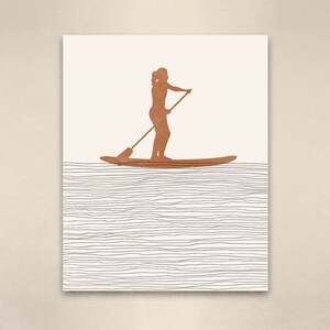 May include: A brown silhouette of a person standing on a paddleboard with a paddle in hand, against a white background with black lines representing water.