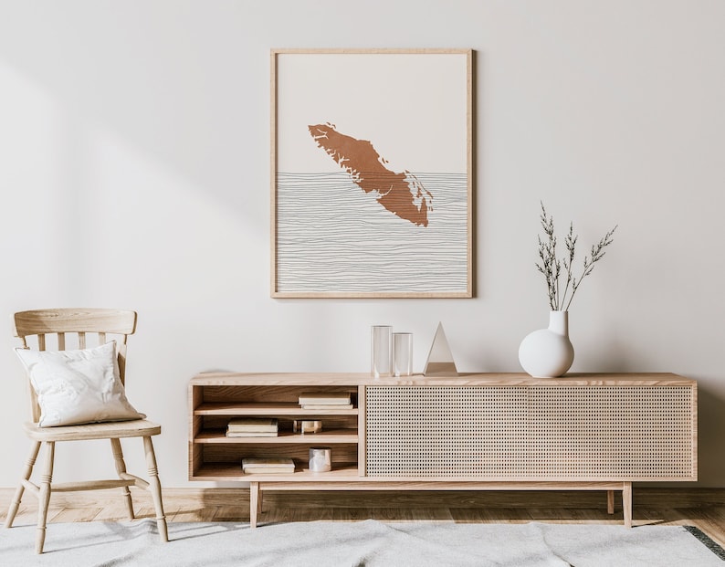 Peut inclure: Un int&eacute;rieur de salon minimaliste avec une console en bois, une chaise et une impression encadr&eacute;e d'un contour brun de l'&icirc;le de Vancouver sur un fond blanc avec des lignes noires.