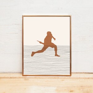 May include: Framed art print featuring a brown silhouette of a person running with a racket. The artwork has a minimalist design with a light peach background and a textured, horizontal line pattern.