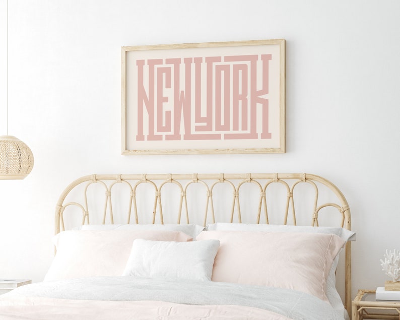 May include: A light pink framed print with the word "NEW YORK" in a bold, stylized font. The print is hanging above a light brown wicker headboard.