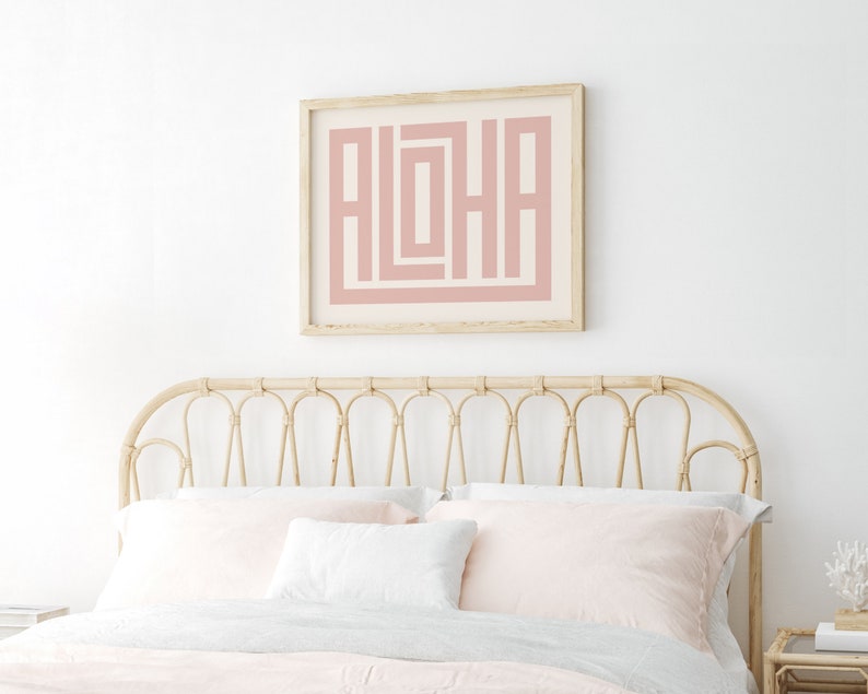 Peut inclure: Une impression g&eacute;om&eacute;trique rose et blanche du mot &laquo;&nbsp;ALOHA&nbsp;&raquo; dans un cadre en bois au-dessus d'une t&ecirc;te de lit en osier brun clair avec une literie blanche et rose.