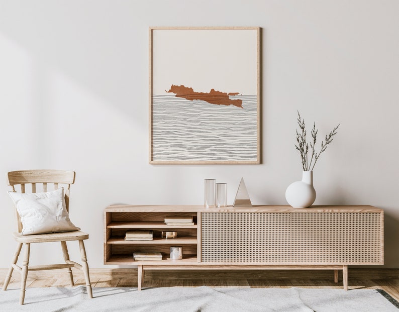 Puede incluir: Un interior de sala de estar minimalista con una consola multimedia de madera, una silla blanca y una impresi&oacute;n enmarcada de una isla marr&oacute;n con l&iacute;neas blancas sobre un fondo beige.