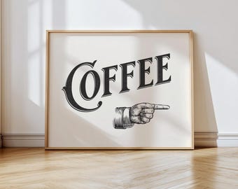 May include: Framed print with the word "COFFEE" in a bold, vintage font. A hand with a pointing finger is illustrated below the text. The artwork is in black and white, set against a cream background, and framed in a light wood.