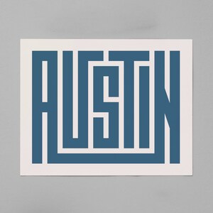 K&ouml;nnte beinhalten: Ein blauer und wei&szlig;er Druck des Wortes "Austin" in einer stilisierten Schriftart. Die Buchstaben bestehen aus Linien und Formen, die ein geometrisches Muster bilden.