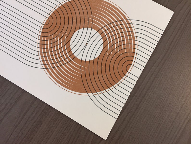 May include: Abstract art print with a brown circle design on a white background. The circle is made up of concentric rings with black lines. The background is a series of black lines.