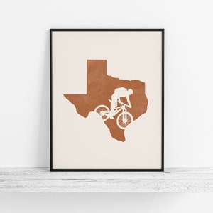 May include: A minimalist print featuring a silhouette of a mountain biker riding over the outline of the state of Texas. The print is in shades of brown and white.