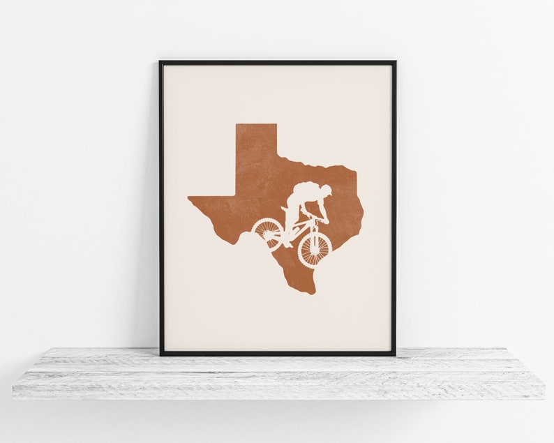 May include: A minimalist print featuring a silhouette of a mountain biker riding over the outline of the state of Texas. The print is in shades of brown and white.