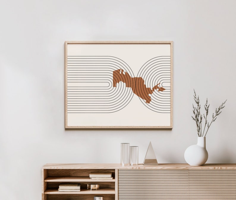 Puede incluir: Una impresi&oacute;n de arte minimalista con una forma abstracta marr&oacute;n rodeada de c&iacute;rculos negros conc&eacute;ntricos sobre un fondo blanco. La impresi&oacute;n est&aacute; enmarcada en un marco de madera claro y est&aacute; colgada en una pared blanca.