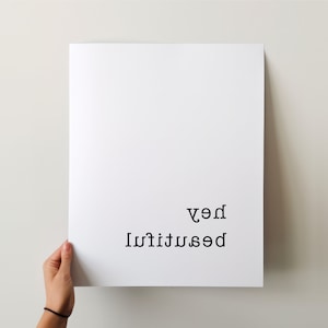 May include: White poster with black text that reads "be beautiful" and "hey" in reverse order.