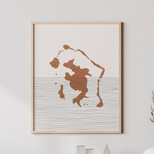 Könnte beinhalten: Ein gerahmter Druck eines minimalistischen abstrakten Designs mit einer braunen Inselform und einer wellenförmigen Linie, die das Wasser darunter darstellt.